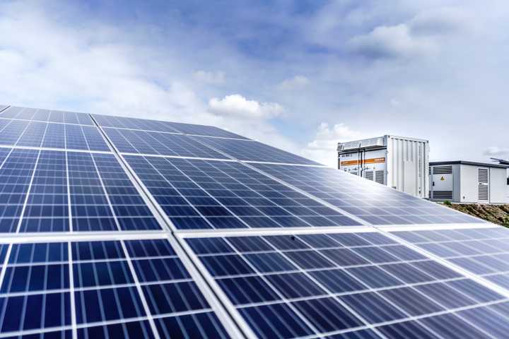 Solar panels with battery storage in the background against a blue cloudy sky